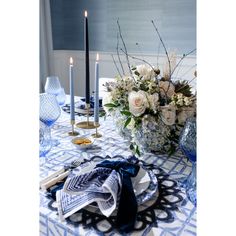 a blue and white table setting with flowers, candles and napkins on the table