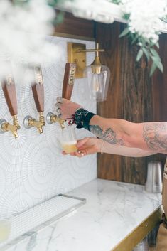 a man holding a beer in front of a wall mounted faucet with three taps