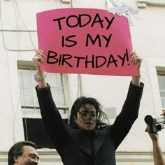 a woman holding up a pink sign that says today is my birthday in front of some people