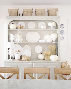 a white china cabinet filled with dishes and pumpkins