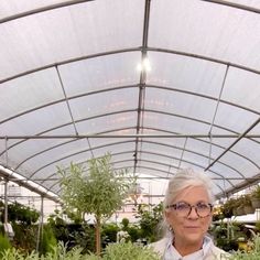 an older woman is standing in a greenhouse holding some plants and looking at the camera