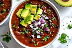 two bowls filled with chili and avocado on top of a white countertop