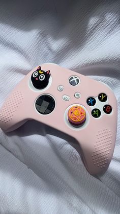 a pink game controller laying on top of a white bed sheet with two black cats