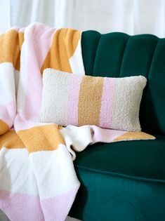 a green couch with a pink and yellow striped blanket on it's back next to a pillow