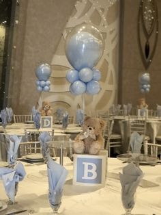 a teddy bear sitting on top of a table next to blue and white balloons in the shape of letters