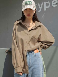 a woman standing in front of a wall wearing a hat and jeans with her hands on her hips