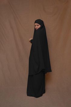 Introducing Black Moira Prayer Umrah Gown with Niqab Feature from Annah Hariri. This beautiful gown is made from high-quality Nada abaya fabric and features super light, stretchy jersey sleeves for ultimate comfort. The elasticated waistband and full skirt ensure a flattering and secure fit, while the khimar can be tied at the back of the head for added coverage.But the best part? This gown can also be transformed into a niqaab with just a few simple stitches. So whether you're performing Umrah, Modest Black Khimar, Long Black Abaya For Eid, Black Long Khimar For Eid, Modest Long Sleeve Black Khimar, Modest Black Long Sleeve Khimar, Black Khimar For Eid, Black Long Sleeve Khimar With Dabka, Long Sleeve Black Khimar For Eid, Traditional Black Dabka Khimar