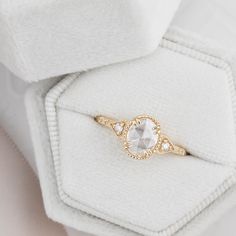 a white and gold ring sitting on top of a white cloth covered box with a diamond in the middle