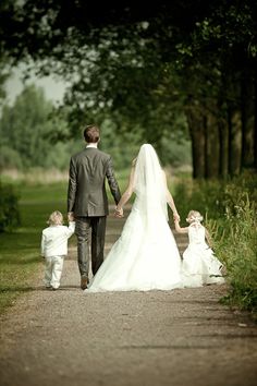 a man and woman holding hands walking down a path with two small children on their laps