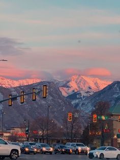 cars are stopped at an intersection with mountains in the backgrouund and traffic lights lit up