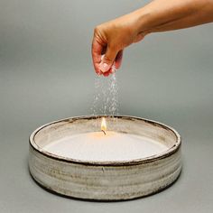 a person is sprinkling sugar on a candle in a tin container with water