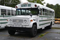 two white buses parked next to each other in a parking lot with trees behind them