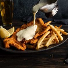 fish and chips being drizzled with mayonnaise on a black plate