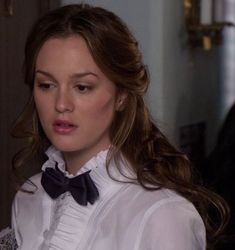 a woman with long hair wearing a white shirt and black bow tie looking at her cell phone