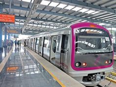 a silver and pink train pulling into a station with people walking on the platform next to it