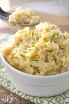 a white bowl filled with rice on top of a green and white table cloth next to a spoon