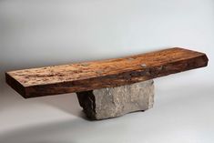 a wooden bench sitting on top of a stone block in front of a white wall