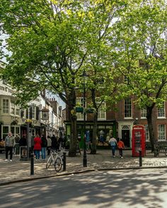 people are walking down the street in front of some buildings and trees with green leaves on them