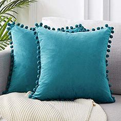 two teal pillows on a couch with a blanket and potted plant in the background