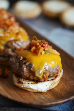 a cheeseburger on a wooden plate with other food items in the back ground