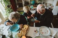 an older couple sitting at a table with plates and bowls in front of them, eating food