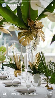 an arrangement of flowers and greenery in vases on a white table cloth with place settings