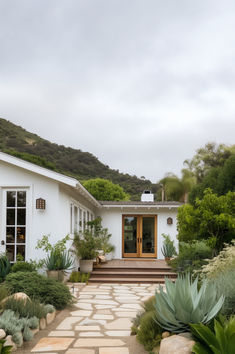 a white house with steps leading to the front door and patio area, surrounded by greenery