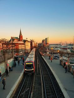 a train station with people walking on the platform and cars parked along the side of the tracks