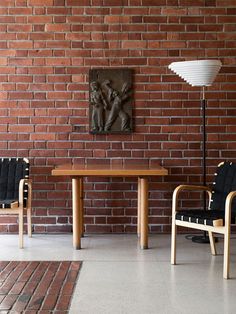 two chairs and a table in front of a brick wall with a painting on it