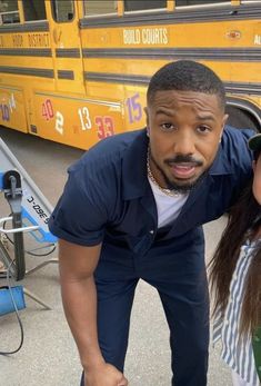 a man standing next to a woman in front of a school bus