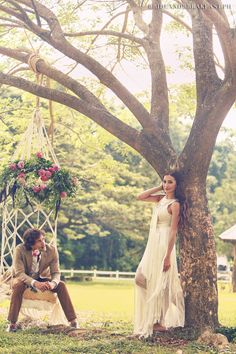 a man and woman sitting in a hammock under a tree