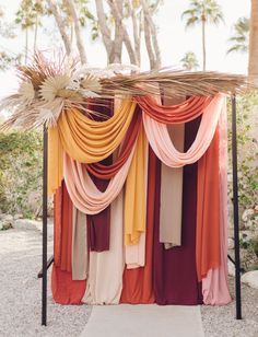 an outdoor ceremony area with colorful drapes and palm trees in the background at sunset