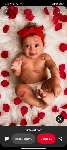 a baby is sitting on a white rug with red petals around it and smiling at the camera