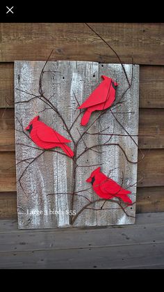 two red birds sitting on top of a tree branch in front of a wooden wall