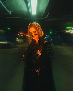 a woman standing in a parking garage holding her hand to her face and looking at the camera