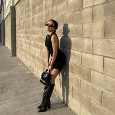 a woman leaning against a brick wall with her hand on the back of her purse