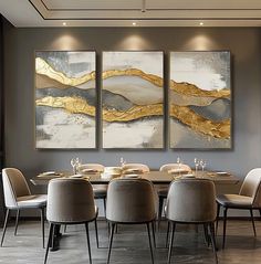 a dining room table with chairs and paintings on the wall above it that have gold leaf accents