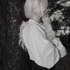 a woman with white hair standing next to a tree