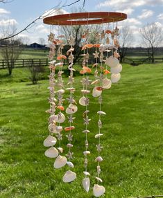 a wind chime with shells hanging from it's side in the grass near a tree