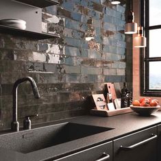 a kitchen with black counter tops and gray tile backsplashing, along with a bowl of oranges on the counter