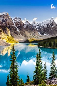 a mountain lake surrounded by pine trees and snow covered mountains in the distance with blue water