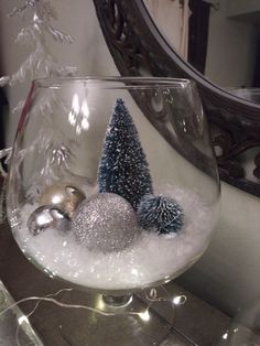 a glass bowl filled with snow and ornaments on top of a table next to a mirror