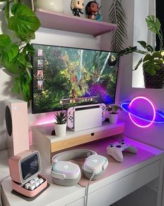 a desk with a monitor, headphones and other items on it in front of a potted plant