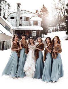 a group of women standing next to each other in front of a barn on top of snow covered ground