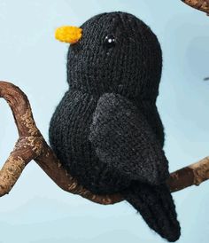 a knitted black bird sitting on top of a tree branch