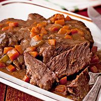 a white plate topped with meat and carrots next to a bowl of soup on top of a wooden table