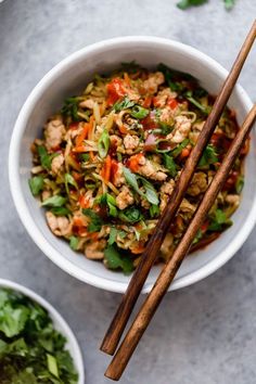 a white bowl filled with stir fry and chopsticks next to another bowl full of food