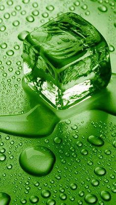 an ice cube sitting on top of a green surface covered in water droplets and drops