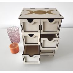 a white cabinet with drawers next to an orange vase and candle on the table in front of it