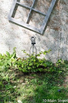 a metal sculpture sitting in the grass next to a wall with a window on it